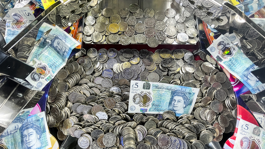 A five pound banknote lies on top of 10 pence coins that are in an amusement arcade slot machine, in Lyme Regis, England, March 20, 2022. /CFP