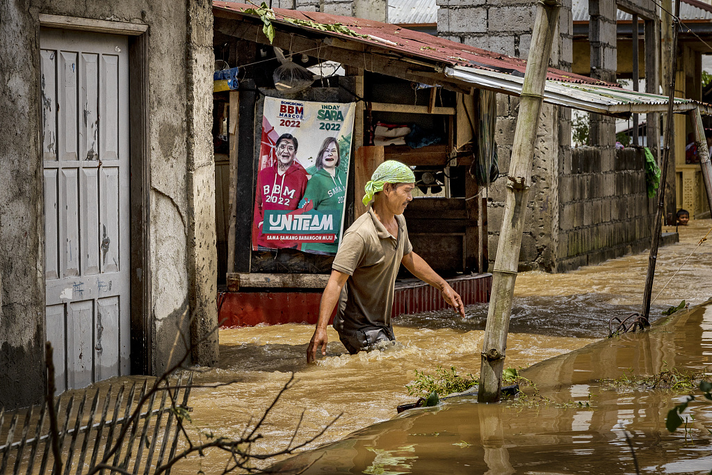 A man wades through floodwaters past an election poster after Super Typhoon Noru hit San Ildefonso, Bulacan province, the Philippines, September 27, 2022. /CFP