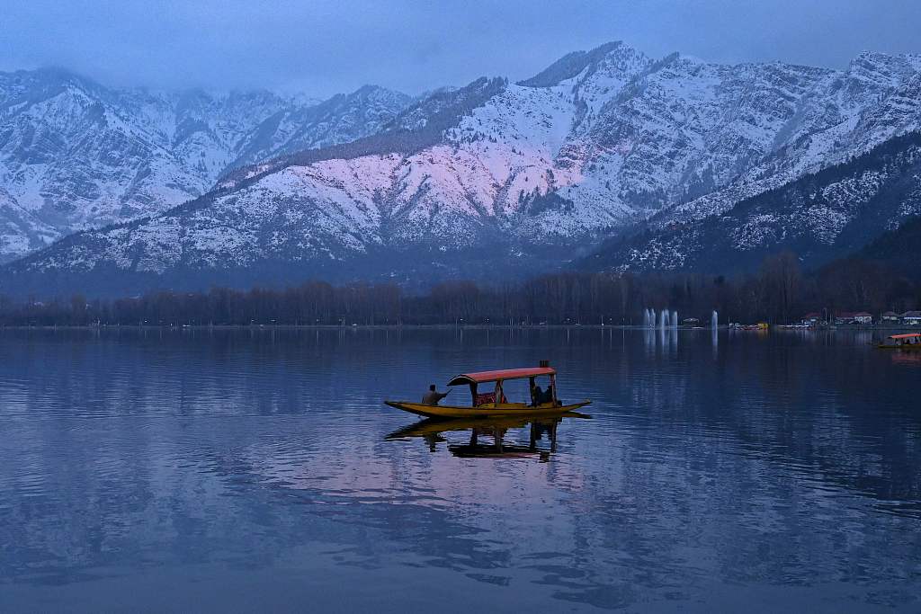 People enjoy a boat ride with snow-covered mountains in the background at Dal Lake in Srinagar, India, January 11, 2022. /CFP