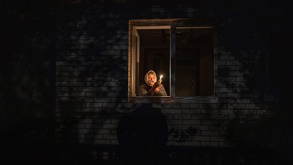 A lady looks out the window while holding a candle for light inside her house during a power outage, Borodyanka, Ukraine, October 20, 2022. /CFP
