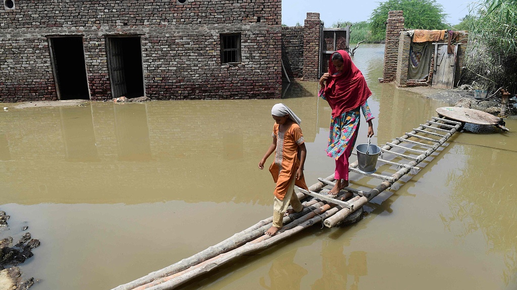 People walk on a temporary bamboo path near their flooded house in southeast Pakistan's Sindh province, August 29, 2022. /CFP