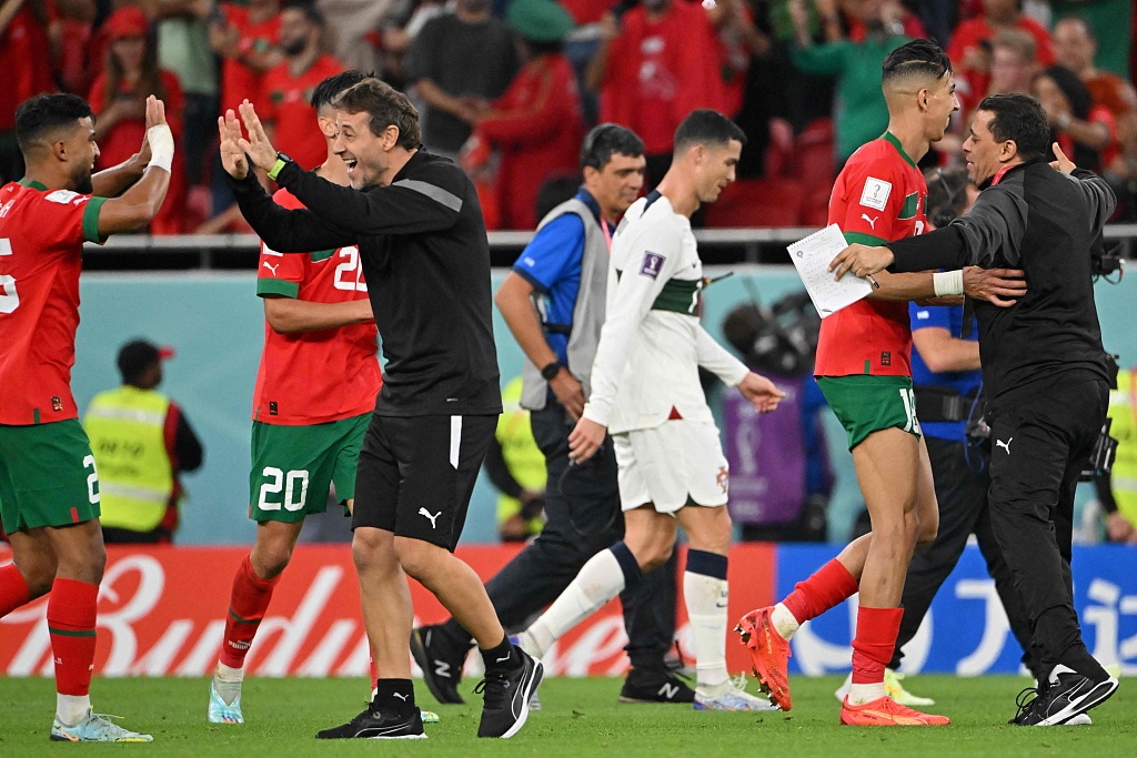 Player and coaches of Morocco celebrate winning the World Cup quarterfinal match against Portugal while an exiting Cristiano Ronaldo is seen in the background in Doha  Qatar, December 10, 2022. /CFP
