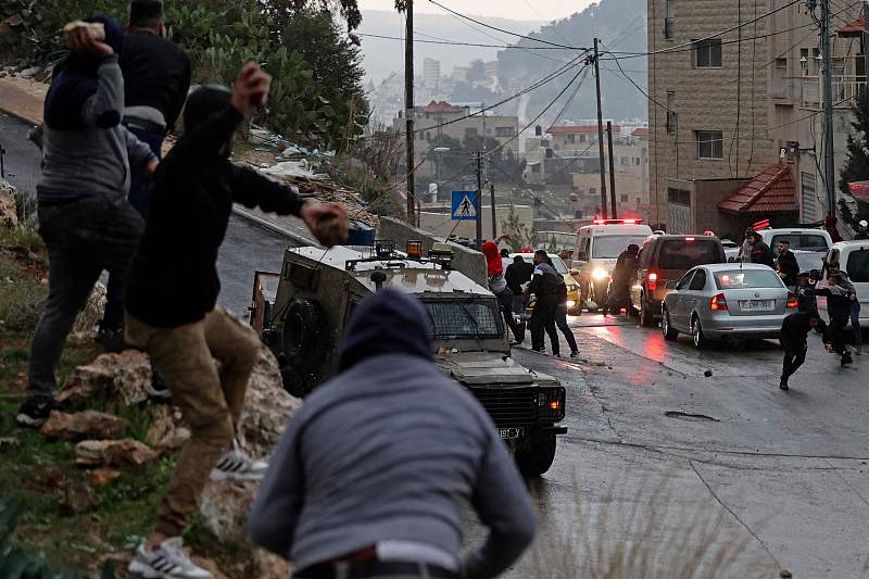 Palestinians hurl stones at an Israeli army vehicle during a raid on Palestinian suspects in Nablus, in the West Bank, December 21, 2022. /CFP