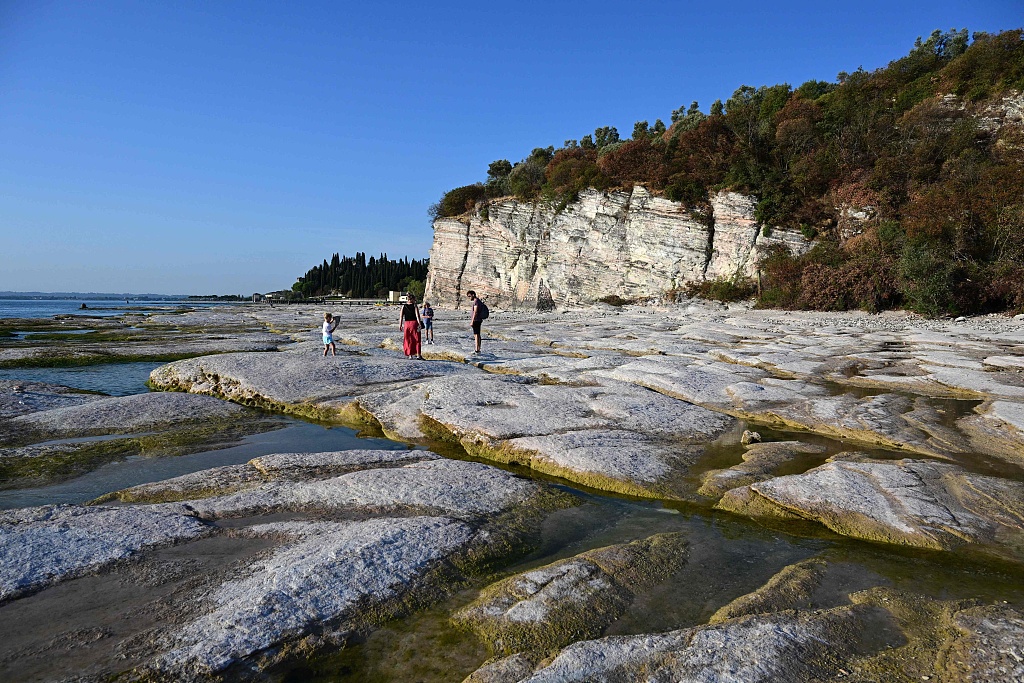 People walk on the rocks of the peninsula of Sirmioneon Lake Garda, northern Italy, as the lake's waters recede due to severe drought, August 16, 2022. /CFP