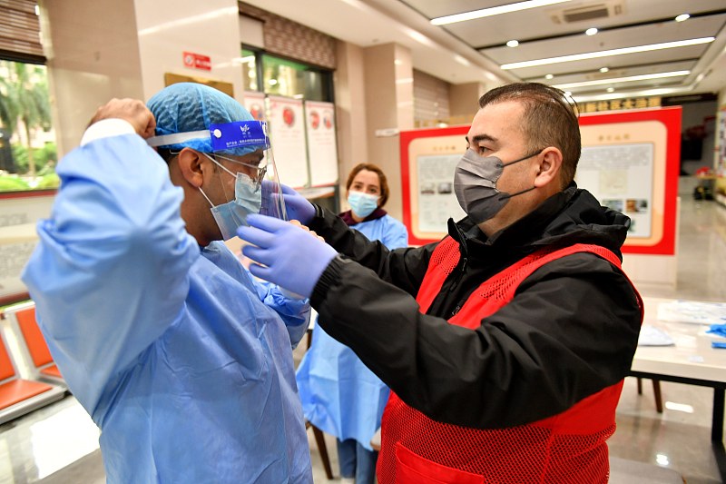 A volunteer from Türkiye (R) helps his colleague wear a medical protective suit at a community nucleic acid testing site in Fuzhou, southeast China's Fujian Province, November 4, 2022. /CFP