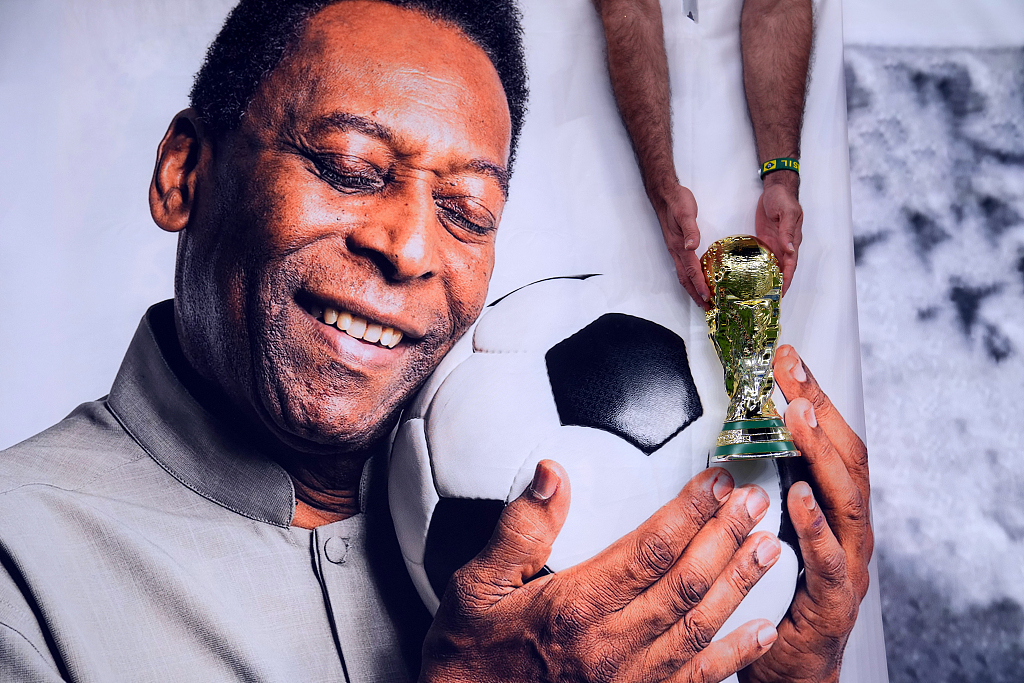 A Brazil fan holding a replica World Cup trophy over a picture of Pele at the Lusail Stadium in Qatar, December 29, 2022. /CFP