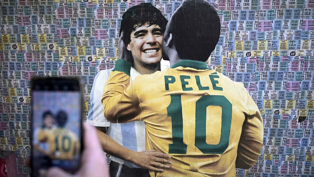 A man takes a picture of a wall depicting an image of late football stars Diego Maradona of Argentina and Pele of Brazil embracing each other, in Buenos Aires, Argentina, just hours after the passing of Pele, December 29, 2022. /CFP