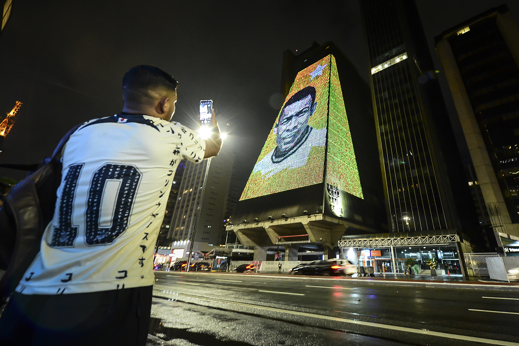 A person takes photos of an image of football icon 'Pele' displayed on a building as a tribute after his passing in Sao Paulo, Brazil, December 29, 2022. /CFP
