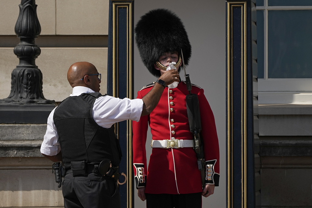 A police officer gives water to a British soldier wearing a traditional bearskin hat, on guard duty outside Buckingham Palace, during hot weather in London, July 18, 2022. Over half of the UK's oldest active weather stations recorded their hottest day ever in 2022, according to UK's climate agency. /VCG