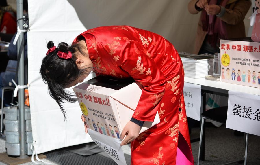 A Japanese girl wearing a red Chinese cheongsam bows deeply to passers-by with a donation box in hands to raise money to help those in China affected by COVID-19 at the Chinese Lantern Festival, Tokyo, Japan, February 8, 2020. /Xinhua