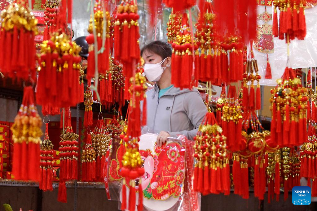 หญิงรายหนึ่งจับจ่ายซื้อของประดับตกแต่งก่อนเทศกาลตรุษจีนในกรุงพนมเปญ กัมพูชา 17 ม.ค. 2566 / ซินหัว