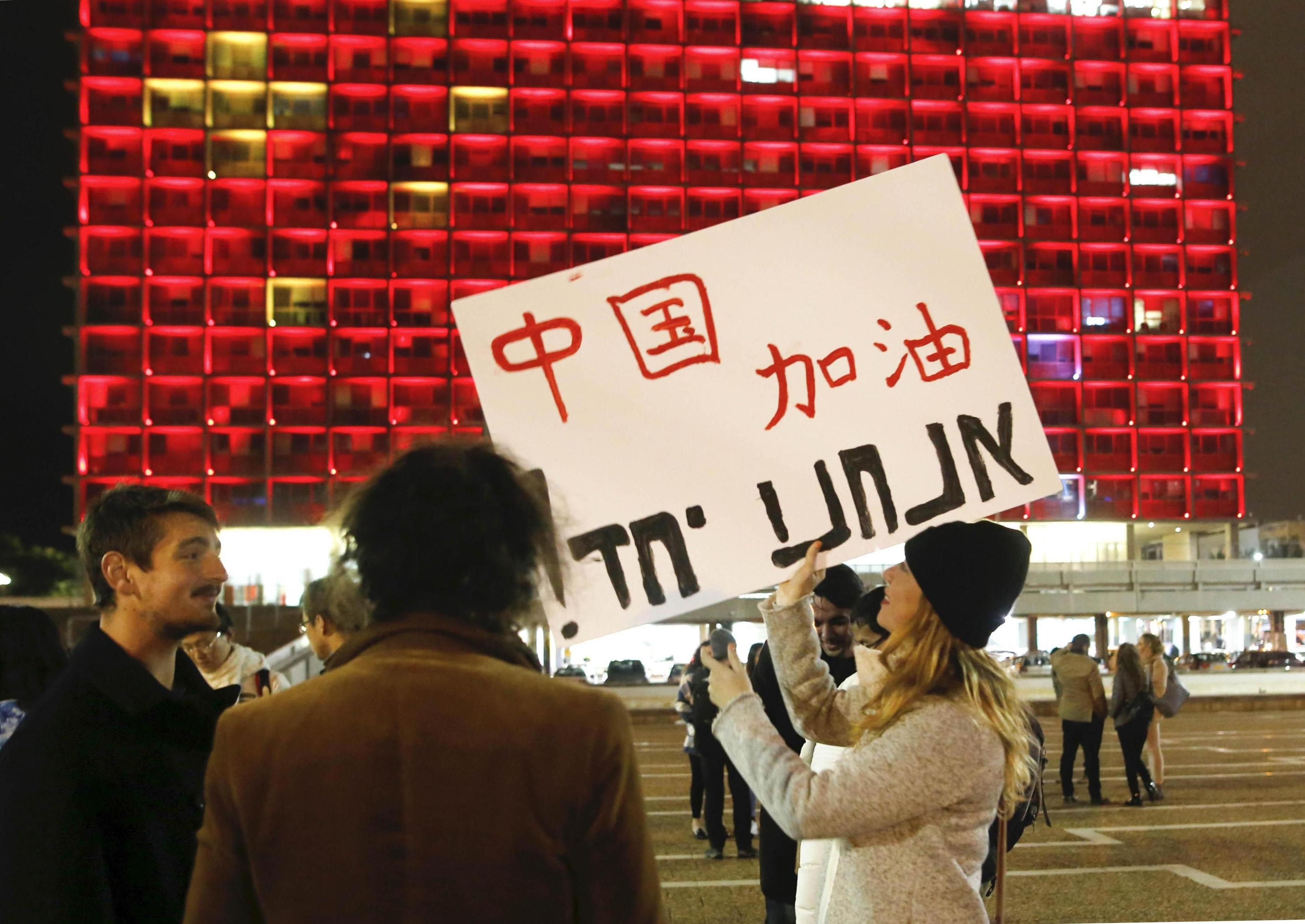 A woman holds a placard to support China in front of the Tel Aviv Municipality Hall lit up with the colors of China's national flag, in solidarity with China's fight against the COVID-19 epidemic, Tel Aviv, Israel, February 11, 2020. /Xinhua