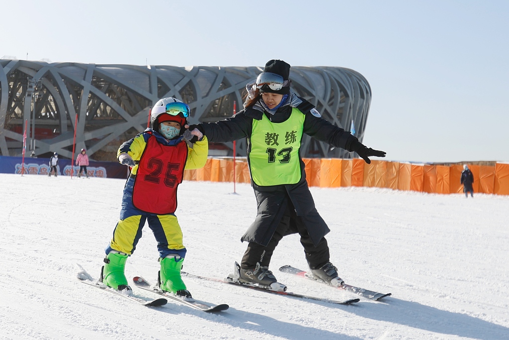 A coach (R) helping a child to ski outside the National Stadium, also known as 