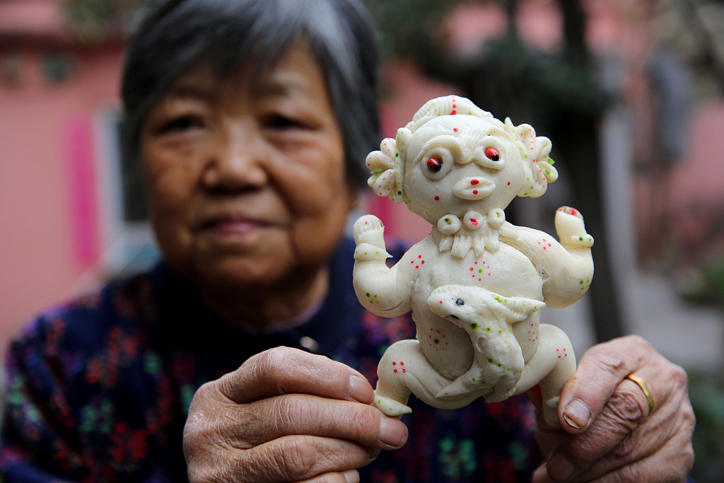 A woman shows her Shenmu dough figurine work. The Shenmu dough figurine is a Shaanxi provincial intangible cultural heritage item, popular in the Shenmu County of Yulin. On July 15th of the traditional Chinese calendar, people bake dough figurines as a sacrifice to the god or send them to relatives and friends. /CFP