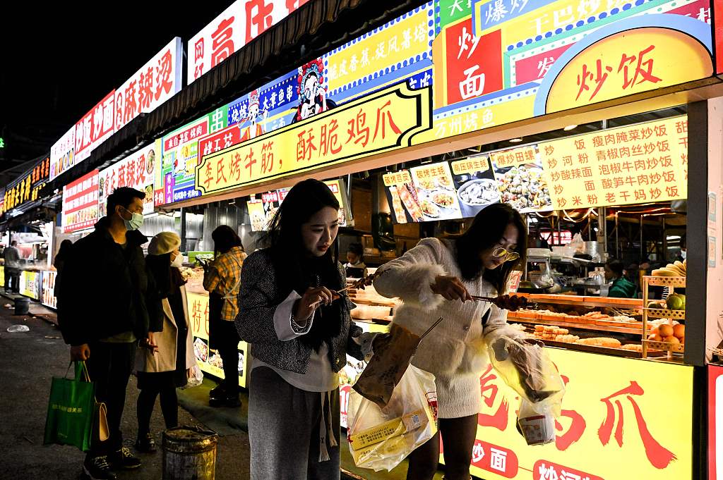 Pedestrians walk and hold food at a night market in Ruili, west Yunnan Province, January 13, 2023. /CFP