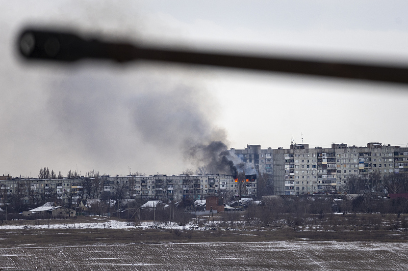 A Ukrainian military vehicle drives by as an apartment building burns in the distance in Bakhmut, Ukraine, February 14, 2023. /CFP