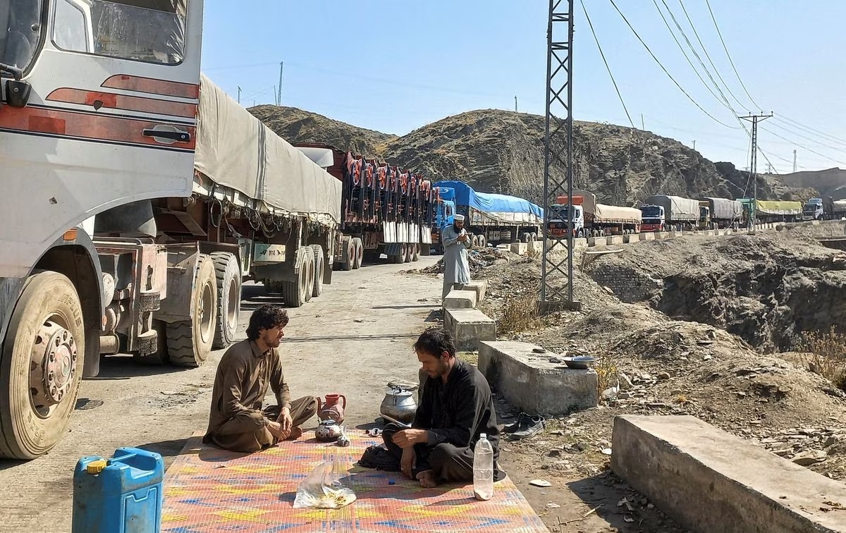 Men sit near a queue of trucks loaded with supplies to leave for Afghanistan, after Taliban authorities closed the main border crossing in Torkham, Pakistan February 21, 2023. /Reuters