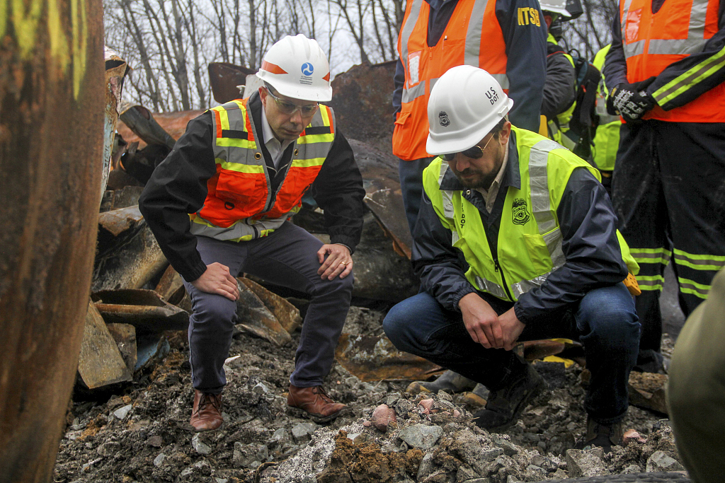 Transportation Secretary Pete Buttigieg (L) and Tristan Brown, deputy administrator of the Pipeline and Hazardous Materials Safety Administration, crouch down to look at part of a burned train-car, in East Palestine, Ohio, U.S., February 23, 2023. /CFP