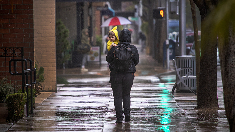 A woman carrying a child walks down the street amidst heavy rain in Pasadena, California, U.S., February 24, 2023. /CFP