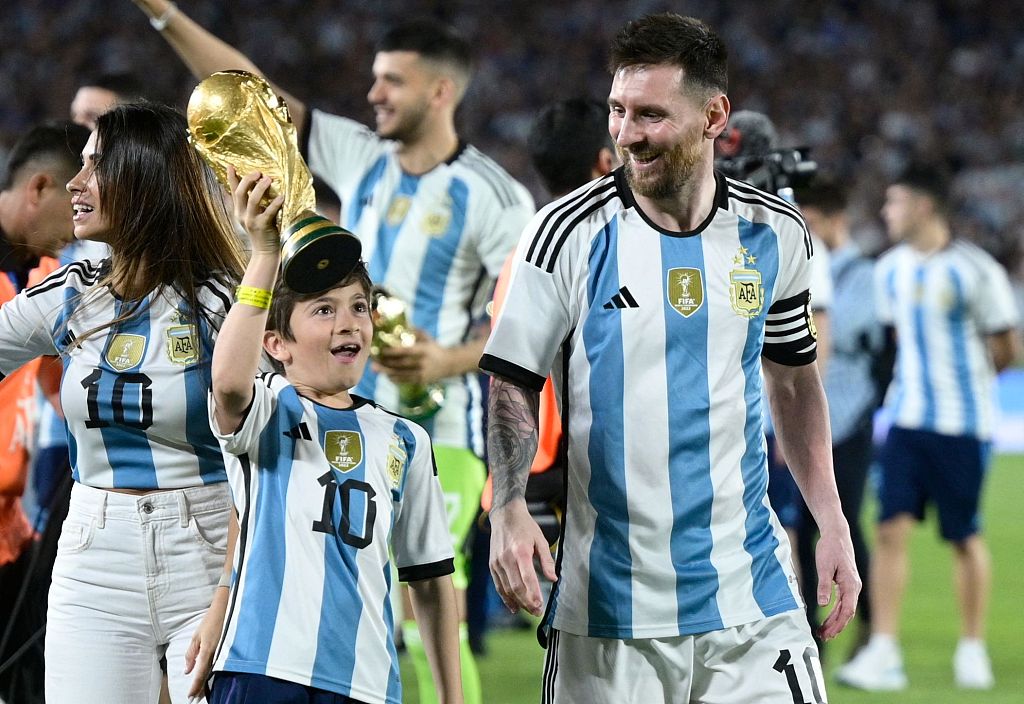 Lionel Messi (R) looks at his son Thiago as he lifts a replica of the World Cup trophy during a celebration ceremony for the World Cup winners in Buenos Aires, Argentina, March 23, 2023. /CFP