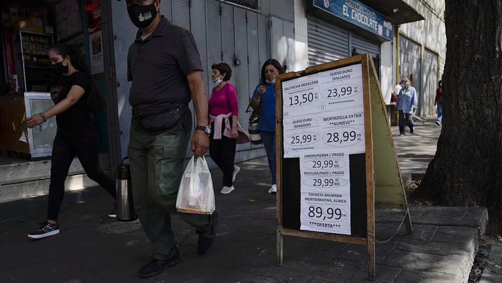 Pedestrians walk past a sandwich board sign displaying the prices of products in bolivars, in Caracas, Venezuela, May 12, 2022. /CFP