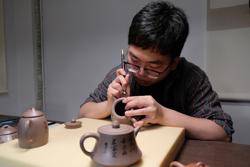 A young man carves poems onto a purple clay teapot at the Yucheng Kiln Cultural Research Institute in Ningbo, Zhejiang. /CFP