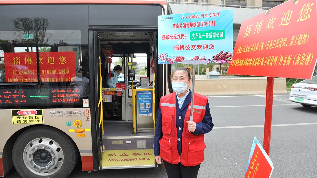 An volunteer holds up a welcoming sign beside a shuttle bus near the Zibo Railway Station, April 14, 2023. /CFP