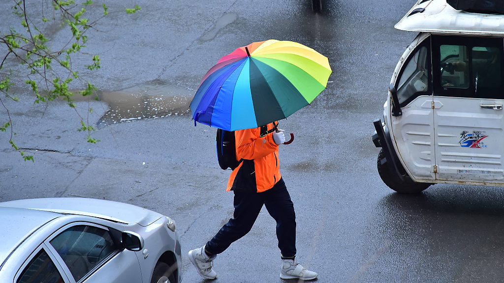 A passenger with an umbrella and warm clothes as the temperature drops and rain falls in Shenyang, northeast China's Liaoning Province, April 20, 2023. /CFP