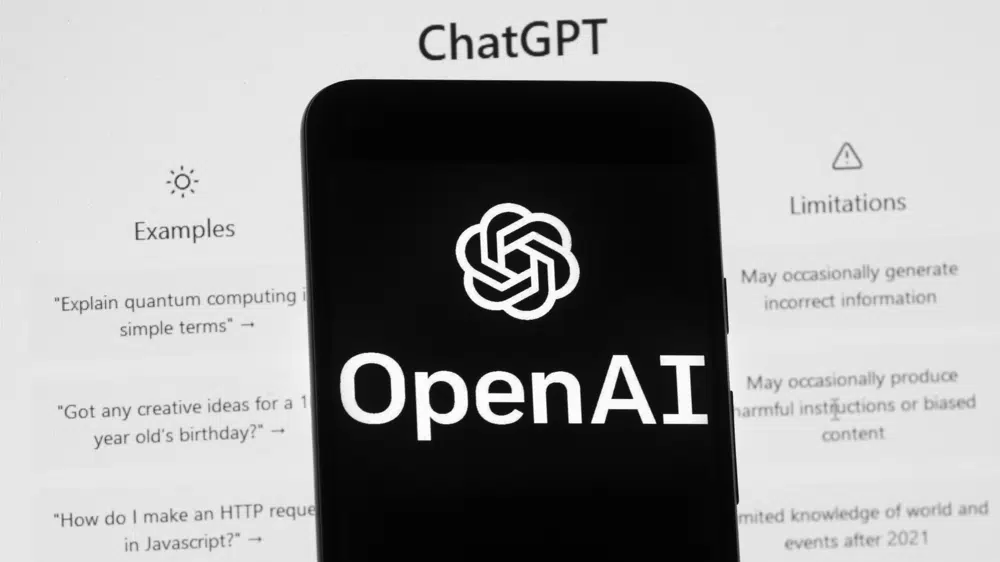 The OpenAI logo is seen on a mobile phone in front of a computer screen which displays the ChatGPT home screen, March 17, 2023. /AP