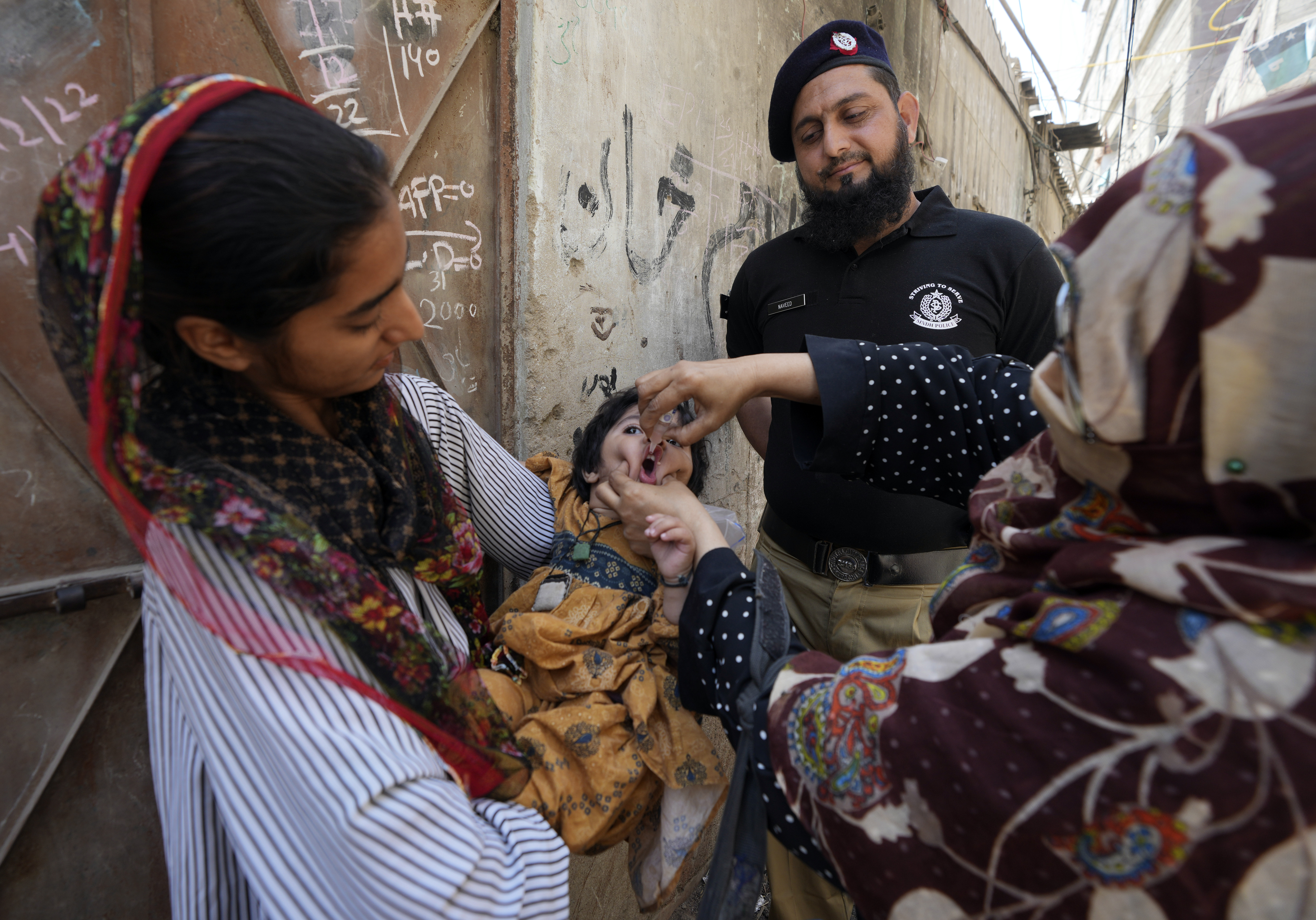 A police officer stands guard while a health worker gives a polio vaccine to a child in Karachi, Pakistan, March 13, 2023. /AP