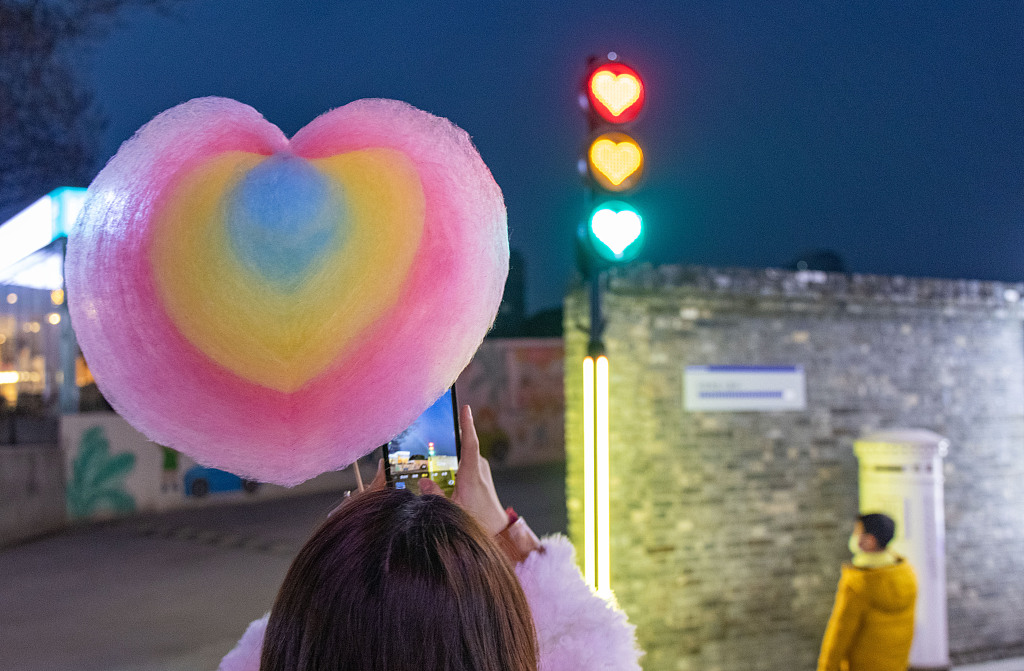 A young woman holding a heart-shaped candy takes photo of a heart-shaped traffic light on a street in Nanjing, Jiangsu, January 7, 2022. /CFP
