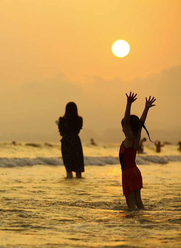 Beachgoers enjoy the view of a sunset in Sanya City, Hainan Province on May 22, 2023. /CFP