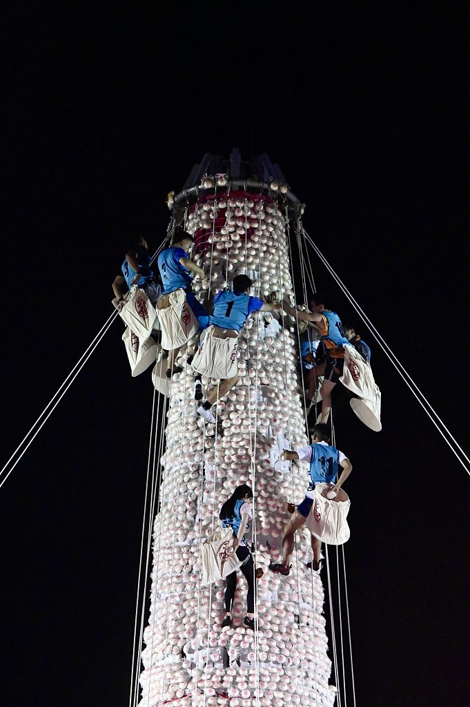 As the clock strikes 12, climbers who have advanced through qualifying rounds in previous weeks race up the bun tower to grab the highest ones during Hong Kong Bun Festival on May 27, 2023. /CFP