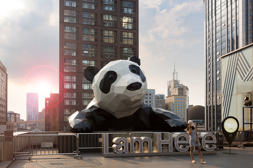 A woman poses for a picture with a giant panda art sculpture at a shopping mall in Chunxilu, Chengdu, Sichuan Province. /CFP