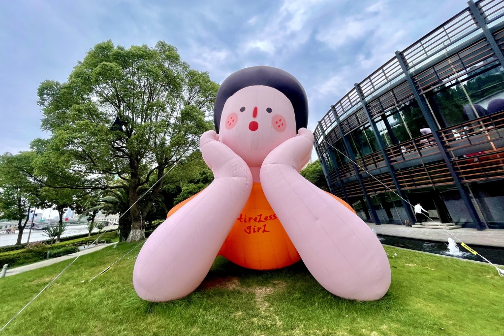 An art installation of a girl resting her chin on her hands while lying on her tummy is photographed on a grass patch in Ningbo, Zhejiang. /CFP