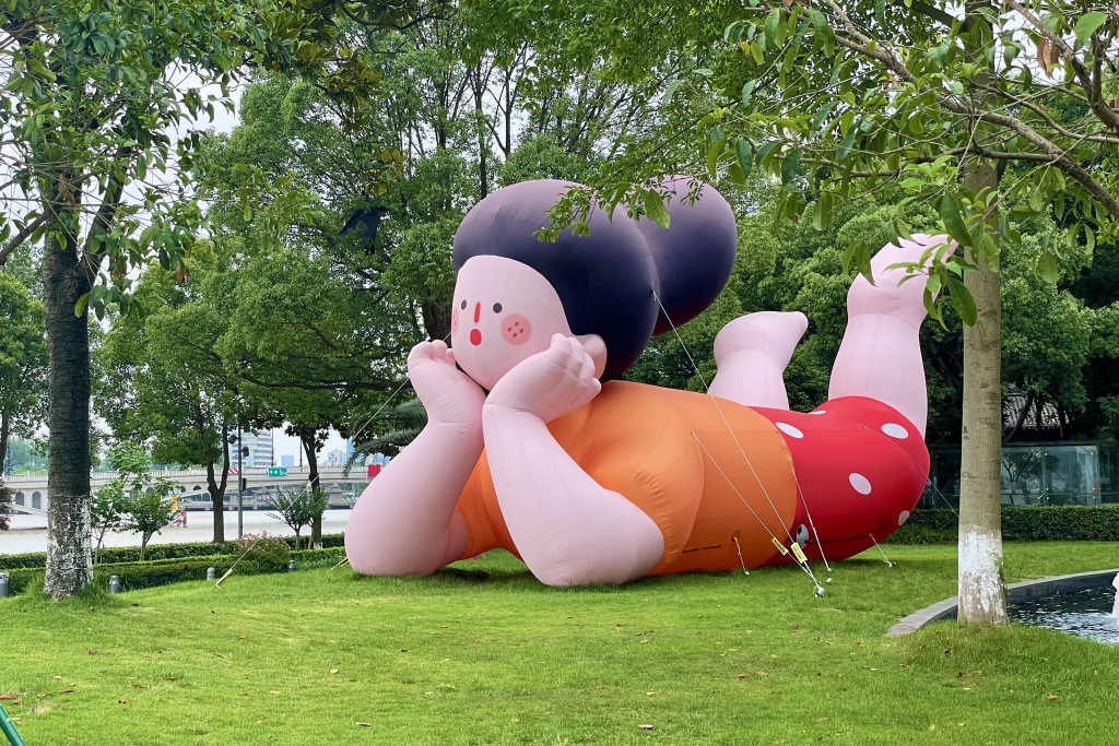 An art installation of a girl resting her chin on her hands while lying on her tummy is photographed on a grass patch in Ningbo, Zhejiang. /CFP