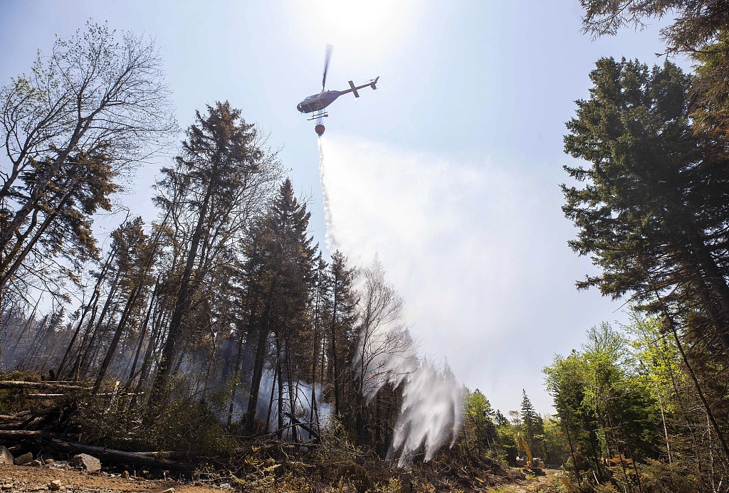 A helicopter contracted by the province drops water on a hot spot in Yankeetown, Nova Scotia, Canada, as an excavator makes a fire break, June 1, 2023. /CFP