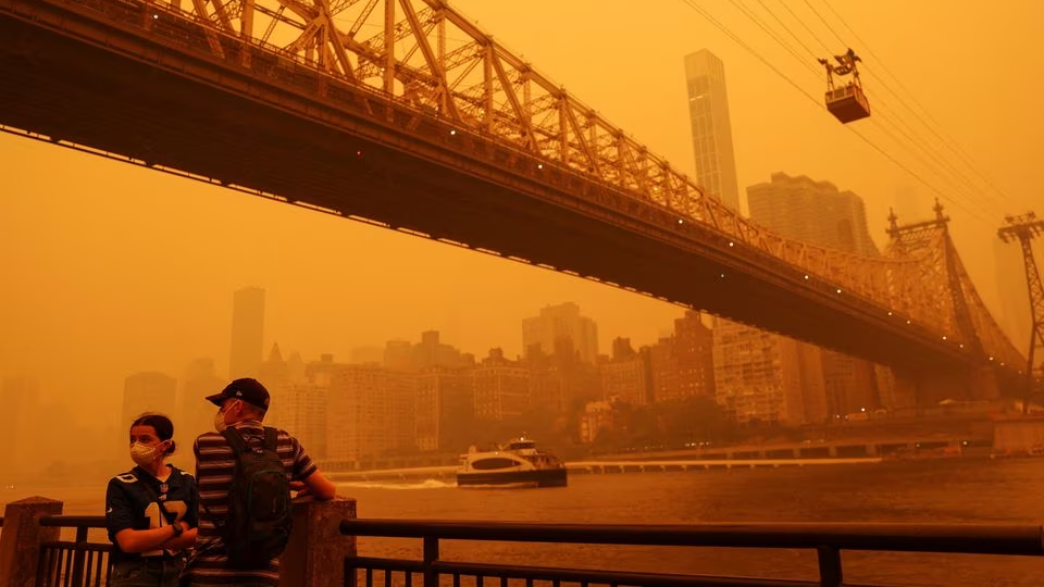 People wear protective masks as the Roosevelt Island Tram crosses the East River while haze and smoke from the Canadian wildfires shroud the Manhattan skyline, June 7, 2023. /Reuters