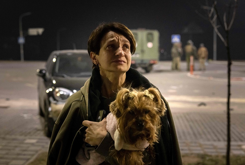 A resident, carriyng her dog, leaves her apartment after a warehouse was hit by debris from a downed rocket in Kyiv on March 20, 2022. /CFP