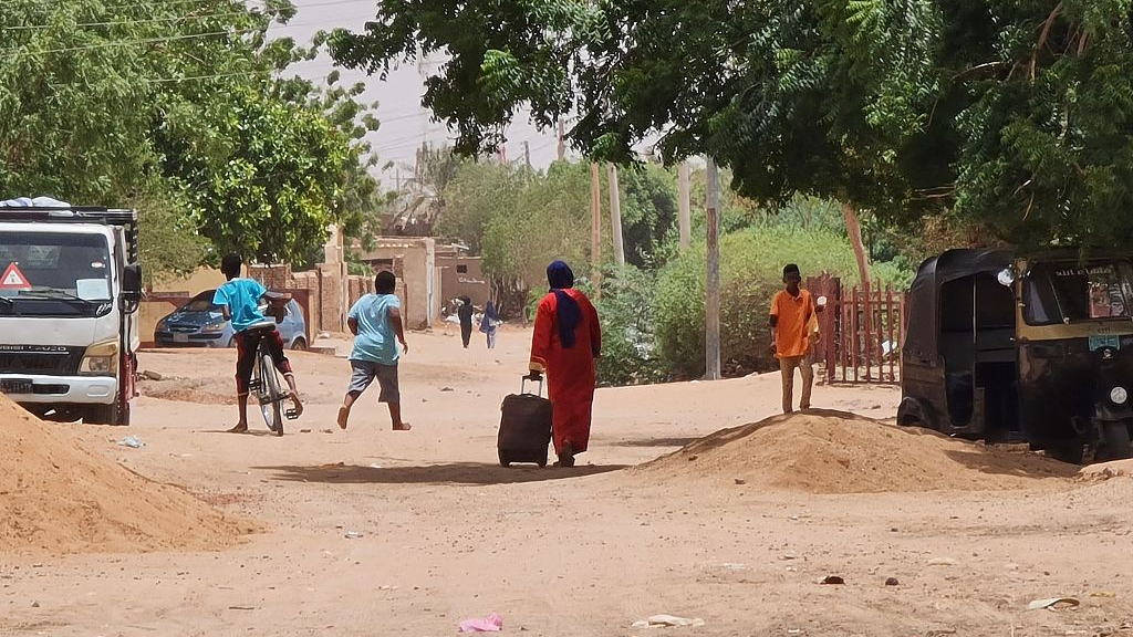 A woman rolls her suitcase as she walks along a dirt road in southern Khartoum amidst ongoing battles in Sudan, June 21, 2023. /CFP