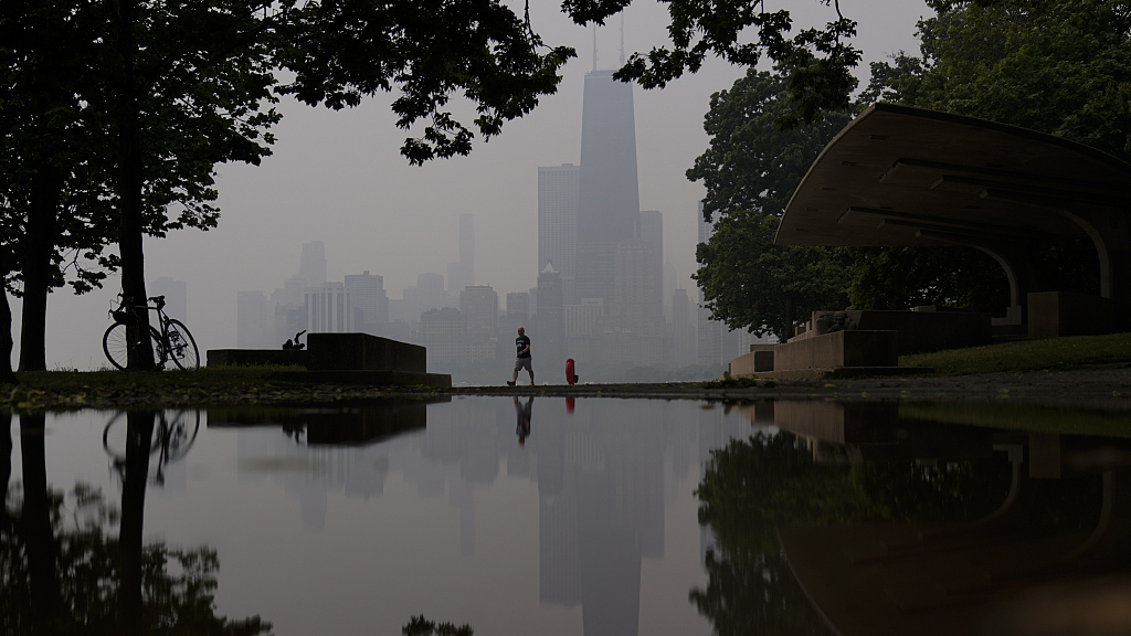 A person walks along the shore of Lake Michigan as the downtown skyline is blanketed in haze from Canadian wildfires, Chicago, U.S., June 27, 2023. /CFP