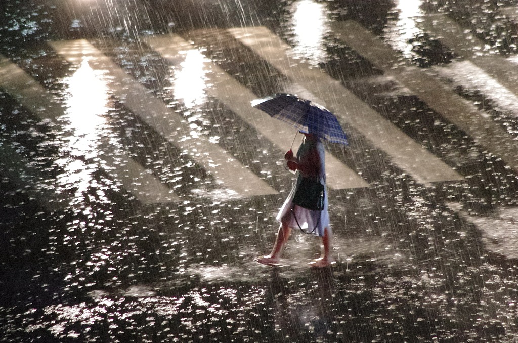 A girl walks in the pouring rain. /CFP