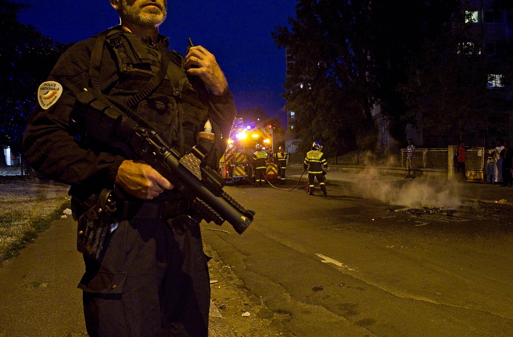 A police officer holds a flash ball as he stands next to firefighters during clashes on June 30, 2023 in Tours, France. /CFP