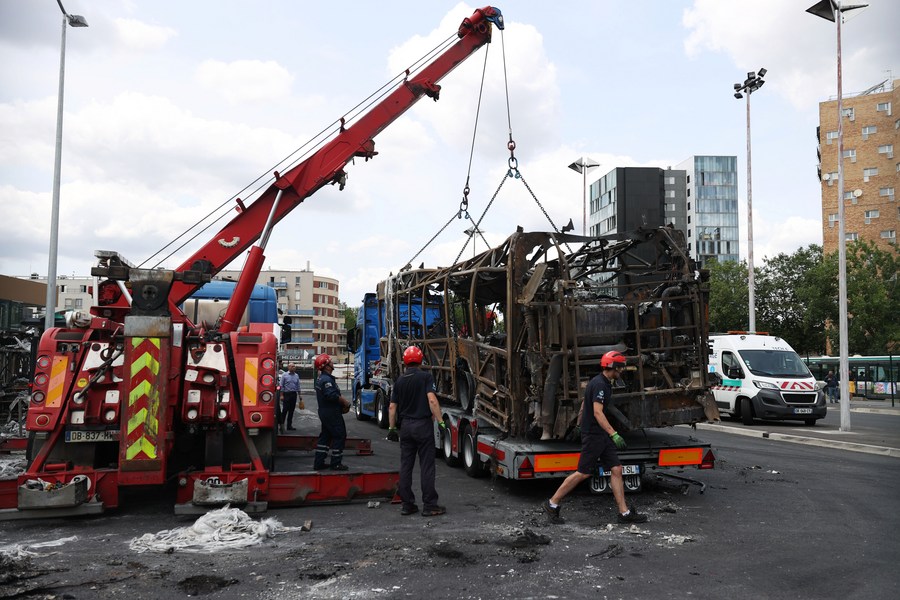 Staff members try to drag away a burnt bus at the Fort d'Aubervilliers bus terminal, in Aubervilliers, north of Paris, France, June 30, 2023. /Xinhua