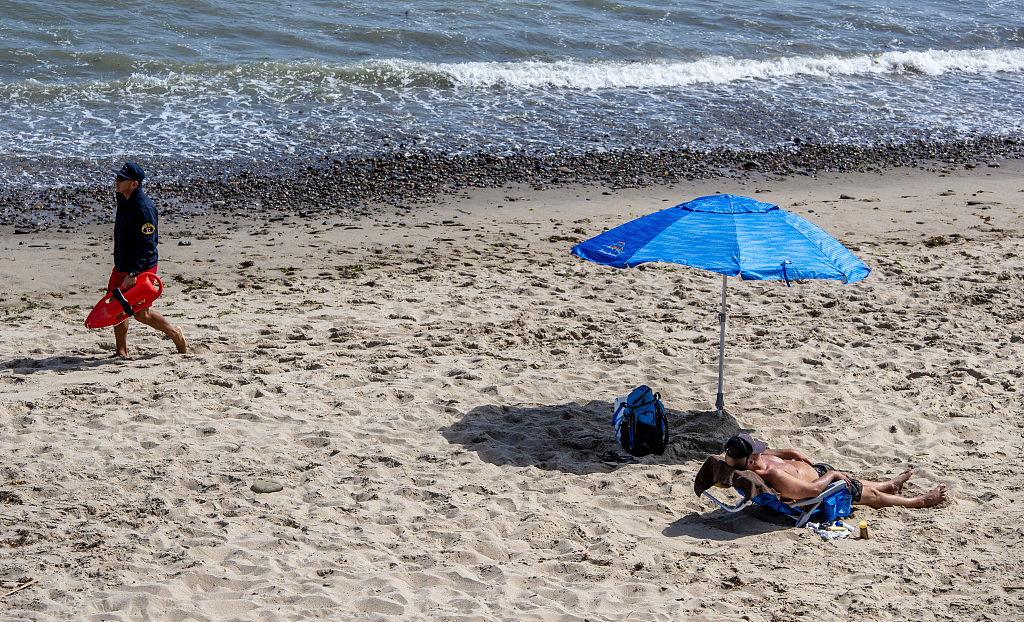 A LA County lifeguard patrols as a man soaks in the sun at Rocky Beach in Santa Monica, the U.S., June 30, 2023. /CFP