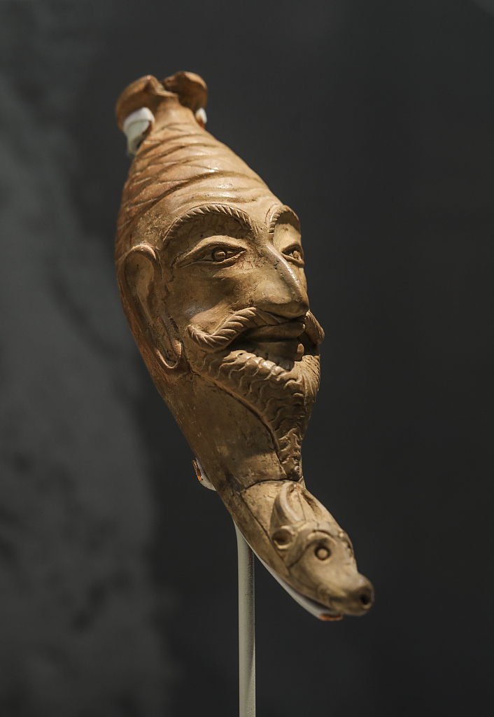A drinking vessel featuring a smiling human head carved on its upper part and a small head of cattle underneath is displayed at a Xinjiang-themed exhibition at the National Museum in Beijing, June 21, 2023. /CFP
