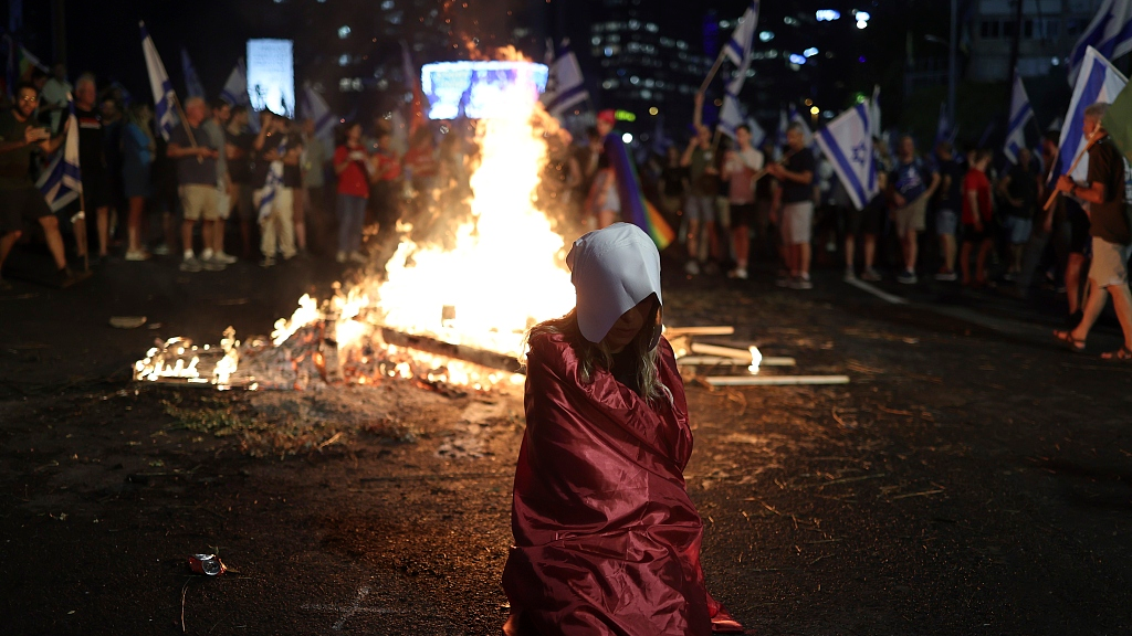 A woman dressed as a character from the Handmaid's Tale TV series sits as demonstrators block the highway during a protest against plans by Prime Minister Benjamin Netanyahu's government to overhaul the judicial system, 5 July 2023, Tel Aviv, Israel. /CFP