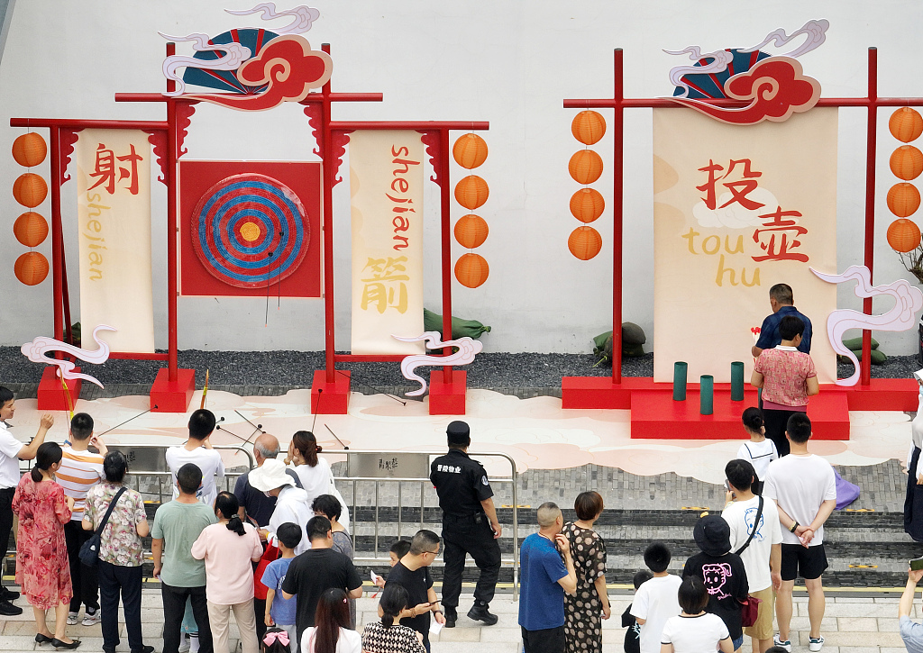 Tourists play the ancient game touhu (throwing arrows into a narrow-neck bottle) at Qingguo Alley in Changzhou, Jiangsu on June 22, 2023. /CFP