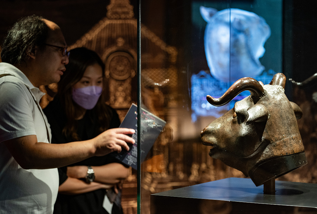 Two visitors stand in front of the bronze ox head sculpture, a treasure of Beijing's Old Summer Palace, on display at the City University of Hong Kong, July 4, 2023. /CFP