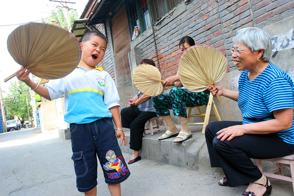 A common sight in China during summertime, senior citizens gather on a street corner to chat with a fan in hand. /CFP